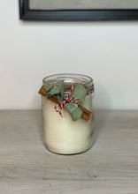 Cargar imagen en el visor de la galería, Vela blanca en un pote de cristal. Lleva de decoración camela en rama, una rama de eucalipto y una cinta de color rojo y blanco.