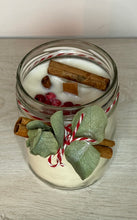 Cargar imagen en el visor de la galería, Vela blanca en un pote de cristal. Lleva de decoración camela en rama, una rama de eucalipto y una cinta de color rojo y blanco. Se ven grosellas y rama de canela en la parte superior de la vela
